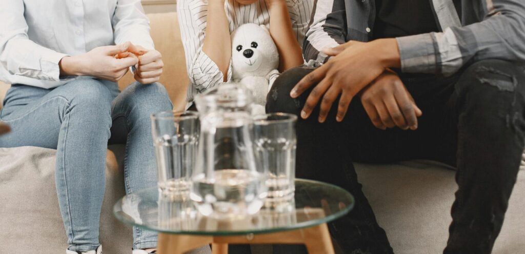 Parents talking to daughter covering ears on sofa.