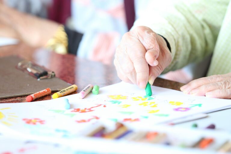 Anonymous senior person with arthritis drawing with green crayon at table in nursing home
