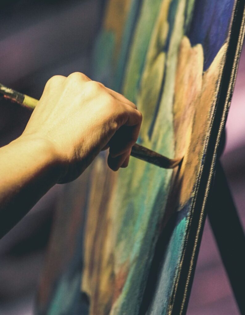 An artist's hand painting a vibrant abstract artwork on a canvas with a brush.